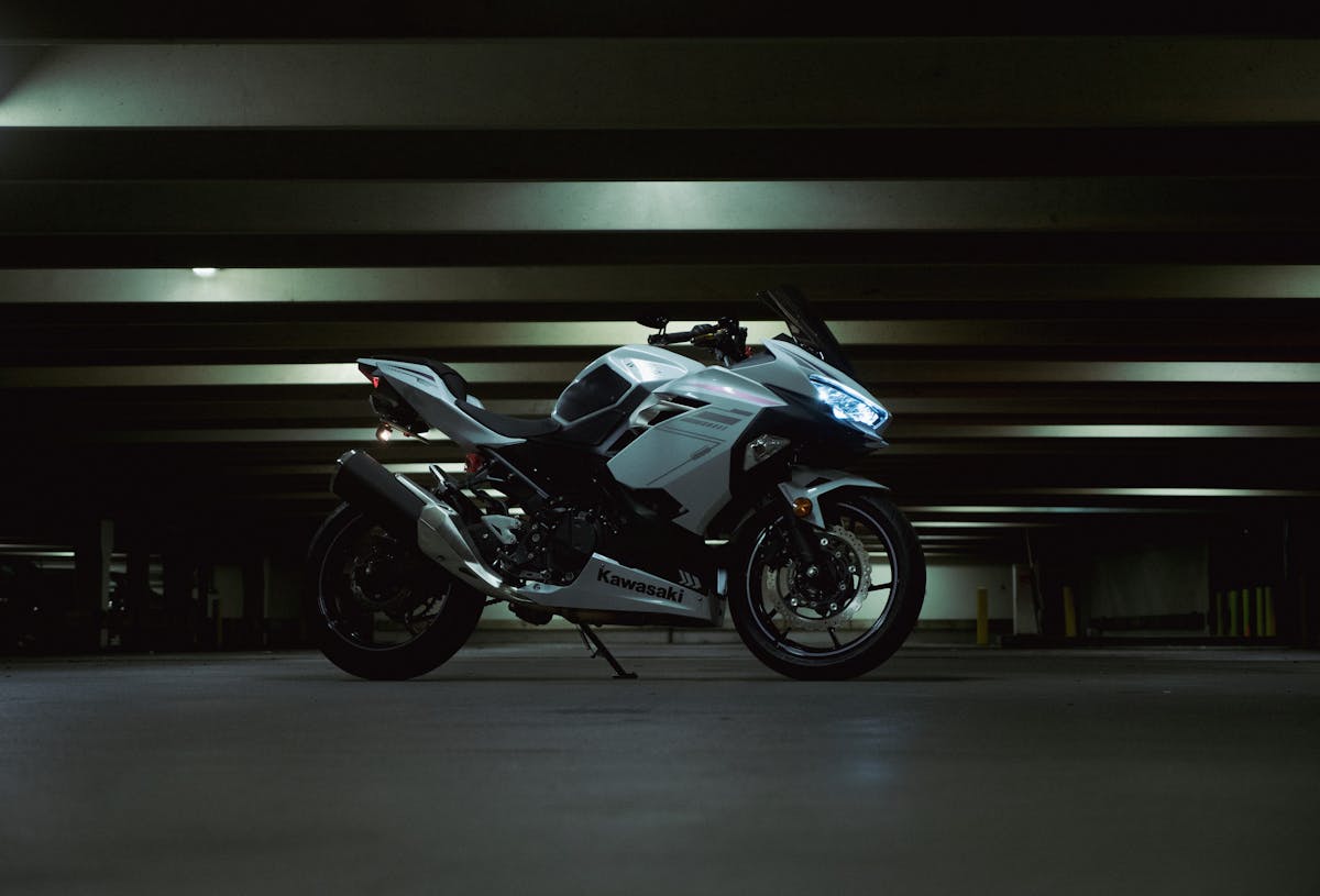 White Kawasaki motorcycle parked in a dark parking garage, showcasing modern design and sleek lines.