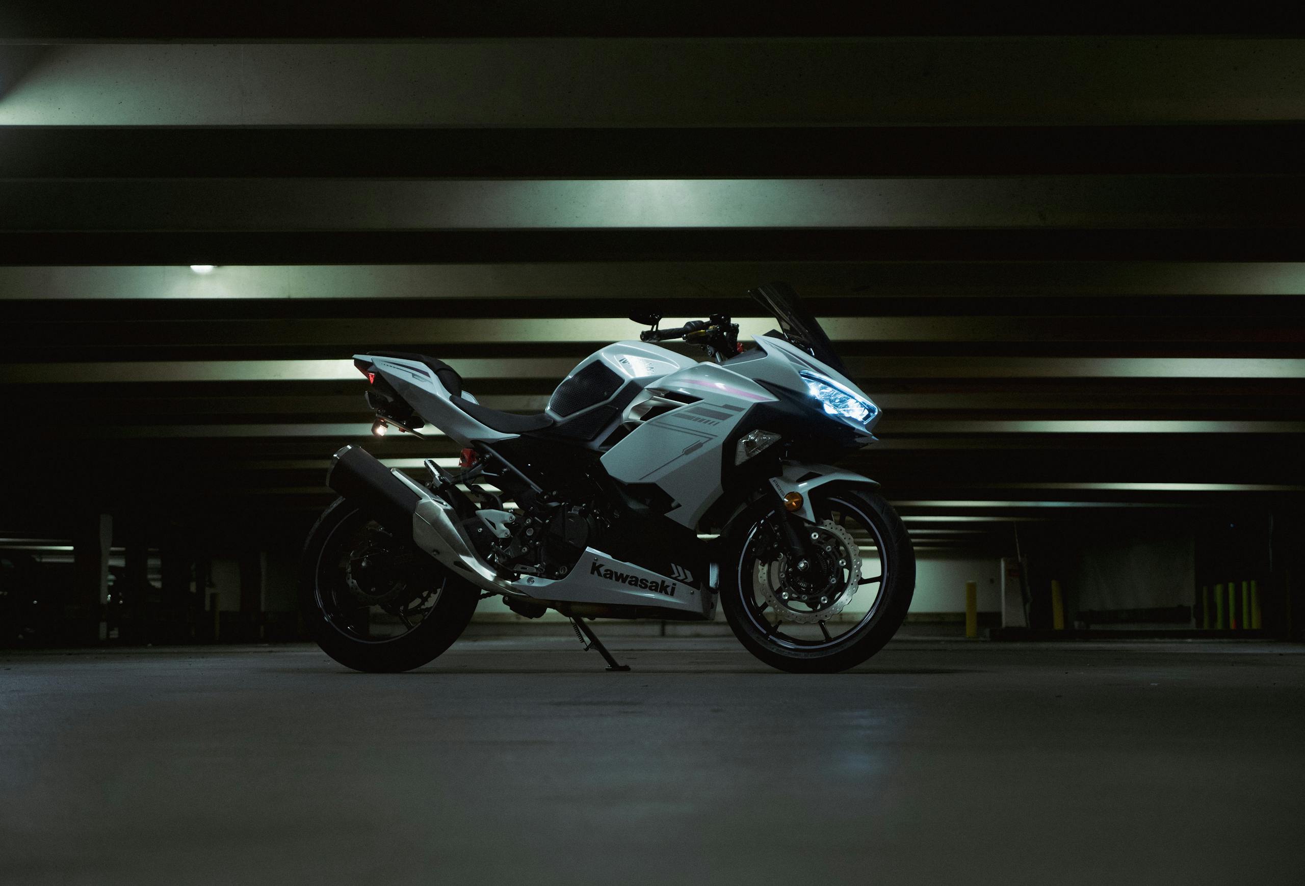 White Kawasaki motorcycle parked in a dark parking garage, showcasing modern design and sleek lines.